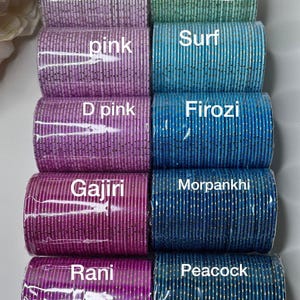 May include: Rows of colorful bangles in shades of pink, blue, and green. Each stack is labeled with a color name in white text. The bangles appear to be made of a shiny, metallic material.