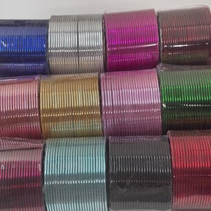 May include: A collection of colorful bangles in various shades, including blue, silver, pink, and green. The bangles are neatly stacked and wrapped in clear plastic, showcasing their metallic sheen. The image displays a variety of colors and styles.