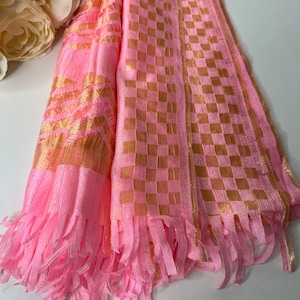 Puede incluir: Bufanda a cuadros rosa y dorada con flecos. La bufanda est&aacute; hecha de una tela suave y ligera y tiene un aspecto delicado y femenino.