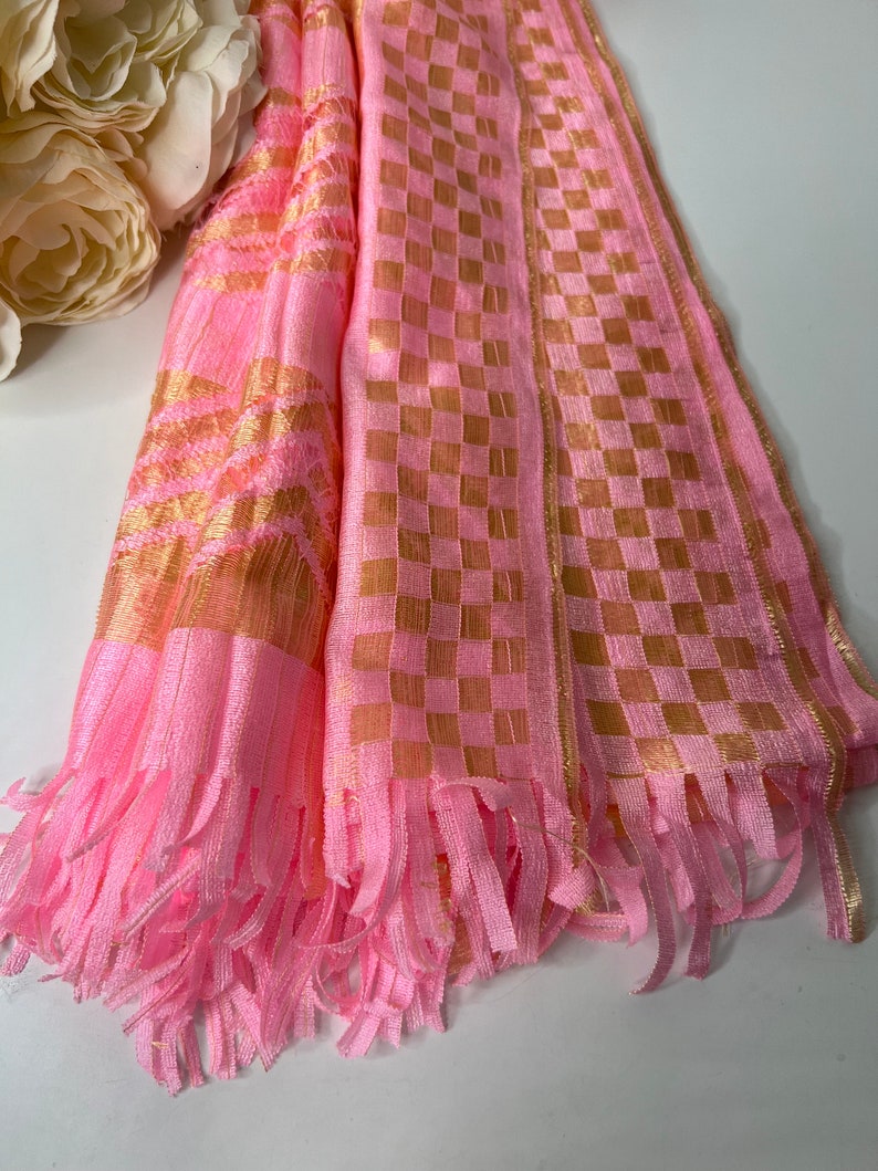 Puede incluir: Bufanda a cuadros rosa y dorada con flecos. La bufanda est&aacute; hecha de una tela suave y ligera y tiene un aspecto delicado y femenino.
