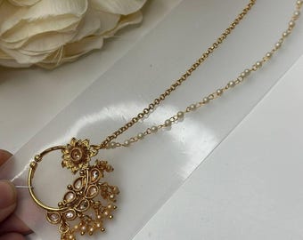 以下が含まれることがあります： 花柄のデザインと真珠のチェーンが付いた金の鼻のリング。鼻のリングは白い背景の上にあります。