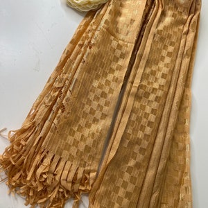 Puede incluir: Una bufanda de cuadros dorados con flecos. La bufanda est&aacute; hecha de una tela suave y ligera y tiene un brillo sutil.