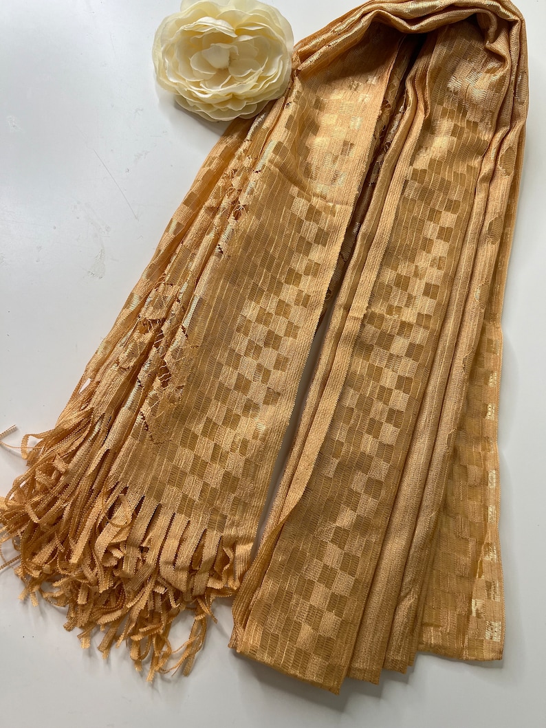 Puede incluir: Una bufanda de cuadros dorados con flecos. La bufanda est&aacute; hecha de una tela suave y ligera y tiene un brillo sutil.