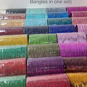 May include: A collection of colorful bangles in various shades, including black, gold, green, red, purple, and blue. The text "Size 2-10 (24 Bangles in one set)" is visible. The bangles are neatly arranged and wrapped in clear plastic.