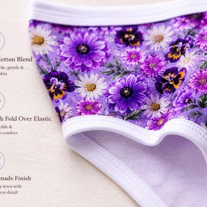 May include: Close-up of purple floral underwear with a white trim. The fabric features a pattern of purple, white, and yellow flowers. The text on the image says "Soft Cotton Blend", "Stretch Fold Over Elastic", and "Handmade Finish".