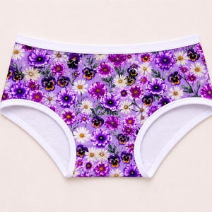 May include: A pair of underwear with a vibrant floral pattern. The underwear features a purple background adorned with various flowers in shades of purple, white, and yellow. The edges are trimmed with white fabric.