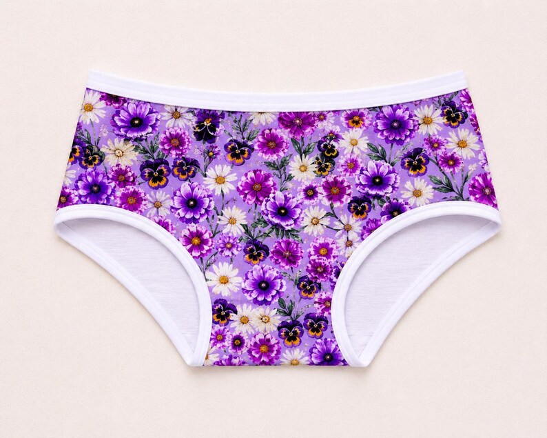 May include: A pair of underwear with a vibrant floral pattern. The underwear features a purple background adorned with various flowers in shades of purple, white, and yellow. The edges are trimmed with white fabric.