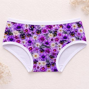 May include: Floral print underwear featuring a vibrant array of purple, white, and yellow flowers against a lavender background. The underwear has a white trim along the edges.