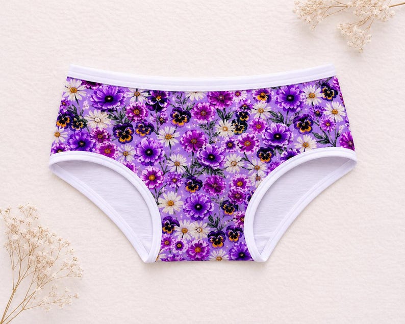 May include: Floral print underwear featuring a vibrant array of purple, white, and yellow flowers against a lavender background. The underwear has a white trim along the edges.