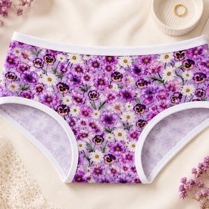 May include: Floral print underwear with a white trim. The underwear features a pattern of purple and white flowers on a light purple background. The underwear is made of a soft, comfortable material.