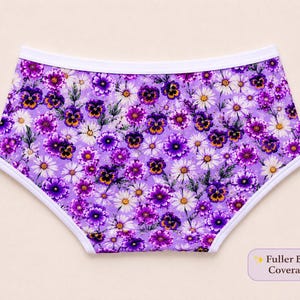 May include: Purple floral underwear with a white trim. The underwear features a pattern of purple pansies and white daisies on a lavender background. The text "Fuller Bum Coverage" is in the lower right corner.