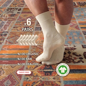 May include: Cream-colored ribbed socks, displayed with six pairs, are shown. The image includes text indicating the socks are 100% organic, raw, and healthy. The socks are on a patterned rug. The image also includes a GOTS label.