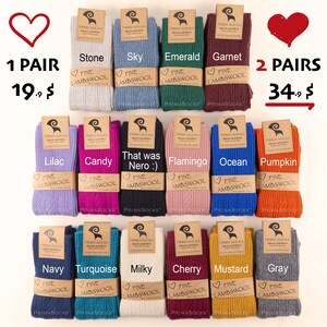 K&ouml;nnte beinhalten: 12 Paar feine Lammwolle Socken in verschiedenen Farben, darunter Stein, Himmel, Smaragd, Granat, Flieder, Bonbon, das war Nero, Flamingo, Ozean, K&uuml;rbis, Marine, T&uuml;rkis, milchig, Kirsche, Senf und Grau. Die Socken sind in zwei Reihen zu sechs angeordnet, mit dem Preis von 19,00 &euro; f&uuml;r ein Paar und 34,00 &euro; f&uuml;r zwei Paar, die &uuml;ber den Socken angegeben sind.