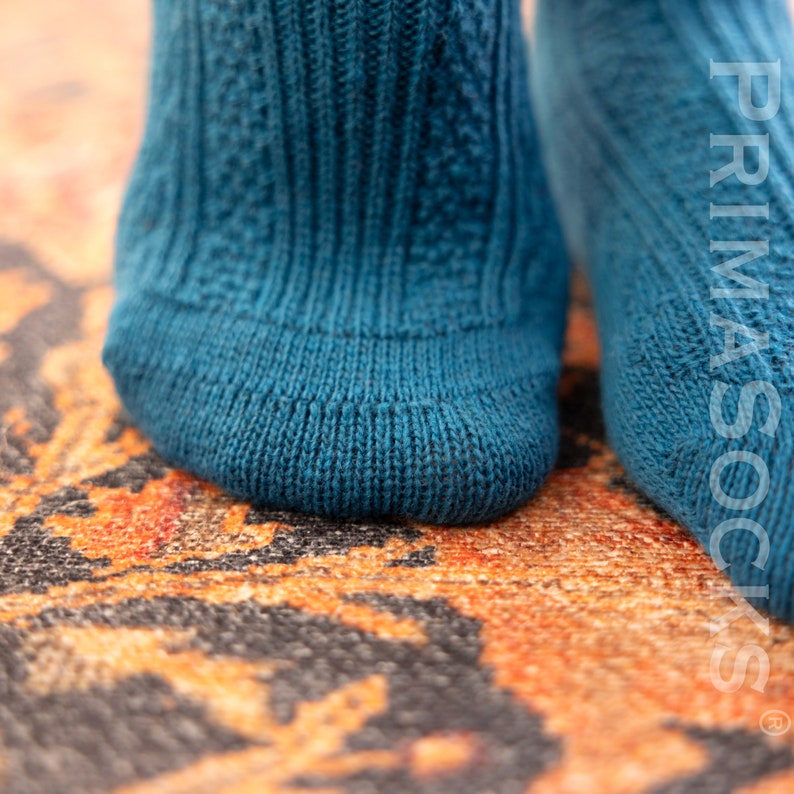 May include: Close-up of a pair of blue knitted socks with a cable knit pattern. The socks are on a patterned rug.