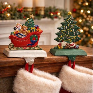 May include: Two Christmas stocking holders. One is a red sleigh filled with toys and a Christmas tree. The other is a green Christmas tree with ornaments and gifts. Both holders have a hook for hanging stockings.