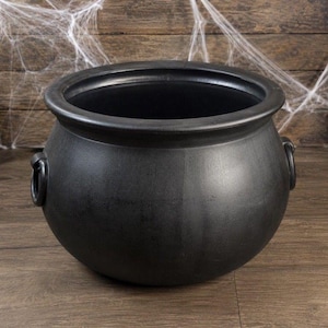 Puede incluir: Un caldero negro mate con una parte superior ancha y abierta y un cuerpo redondeado. El recipiente cuenta con dos asas laterales circulares unidas al exterior. La superficie tiene un acabado liso y uniforme, con un borde grueso y prominente.