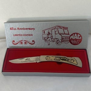 May include: A silver-colored pocket knife with a gold-colored design, presented in a silver box with red interior. The box reads "45th Anniversary Limited Edition" and features a truck illustration. The knife is marked "MAC Limited Edition".
