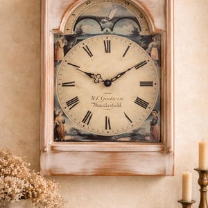 May include: A distressed white wooden wall clock with a painted face featuring Roman numerals and the text "W.L. Godwin Macclesfield." The clock has a landscape scene and figures on the face and top, with a curved top section.