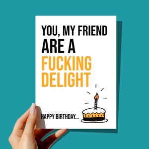May include: A white card with black text that reads "You, my friend are a fucking delight. Happy birthday..." with a hand-drawn illustration of a birthday cake with a lit candle on top.