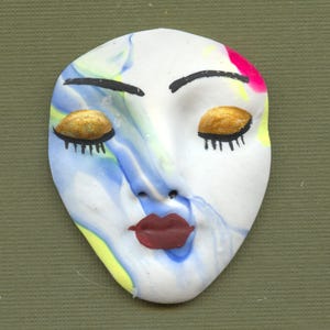 May include: A white, oval-shaped mask with closed eyes and a red pout. The mask features gold eyelids, black eyebrows and eyelashes, and a swirled design of blue, yellow, and pink paint. The mask is likely handmade.