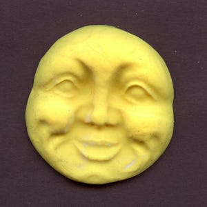 May include: A yellow, smiling moon face sculpture with detailed facial features. The moon has a cheerful expression with closed eyes and a wide smile. The sculpture is a bright yellow color and appears to be made of a solid material.
