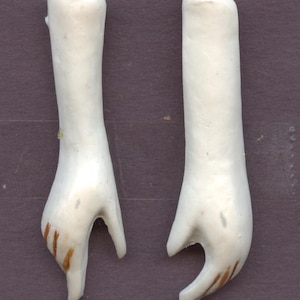 May include: Two white porcelain doll arms with painted brown lines on the hands.