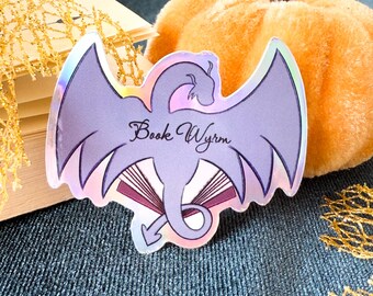 May include: A holographic sticker featuring a purple dragon curled around a book with the text "Book Wyrm" in a cursive font.