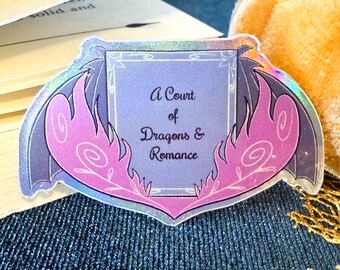 May include: A holographic sticker with a purple and pink design. The sticker features a frame with the text "A Court of Dragons & Romance".