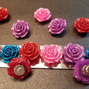 May include: Assortment of 10 glitter rose magnets in various colors, including red, pink, purple, blue, and teal. The magnets are approximately 1 inch in diameter and have a flat back with a silver magnet.
