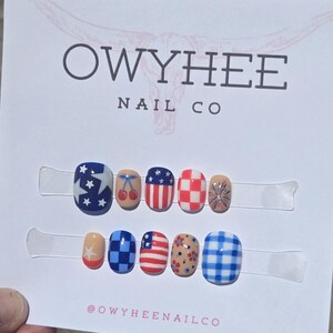 May include: A set of ten press-on nails displayed on a white card labeled OWYHEE NAIL CO. The designs include American flag patterns, red cherries, red and white checkers, blue and white gingham, floral motifs, and star patterns in red, white, and blue.
