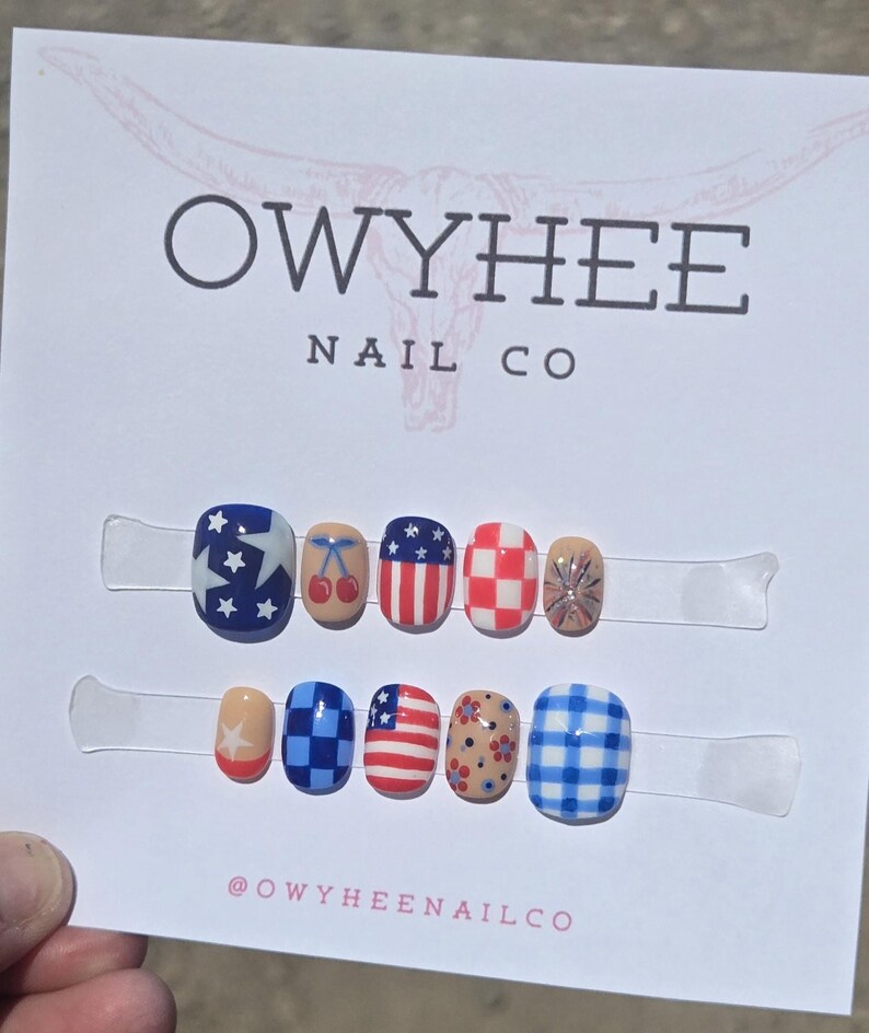 May include: A set of ten press-on nails displayed on a white card labeled OWYHEE NAIL CO. The designs include American flag patterns, red cherries, red and white checkers, blue and white gingham, floral motifs, and star patterns in red, white, and blue.