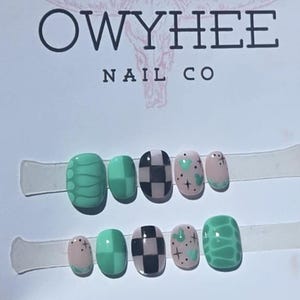 May include: A set of ten press-on nails displayed on a white card labeled OWYHEE NAIL CO. The nails feature various designs including green snake skin patterns, solid green squares, black and white checkerboards, and light pink with green hearts.