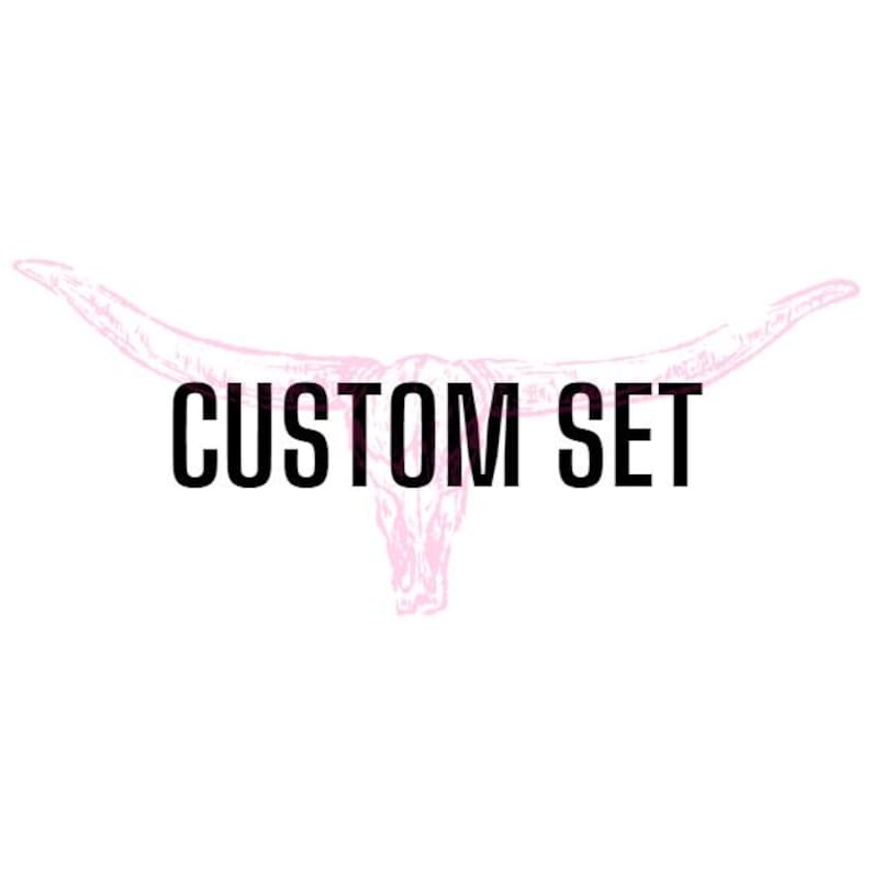 May include: A light pink line drawing of a longhorn steer skull centered on a plain white background. The words CUSTOM SET are printed in bold black capital letters across the center of the skull illustration, overlaying the pink line art.