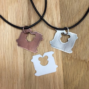 May include: Three necklaces with a slice of bread pendant. The pendants are made of copper, silver, and white metal. The necklaces are on a wooden surface.