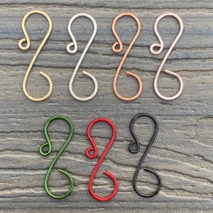 May include: Assortment of eight wire ornament hooks in various colors, including gold, silver, copper, rose gold, green, red, and black. The hooks are all the same size and shape, with a simple, elegant design.
