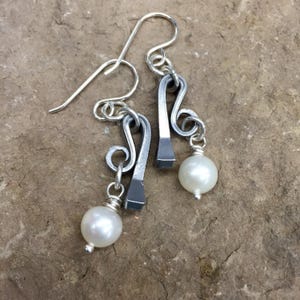 May include: Silver earrings with a horseshoe design and a white pearl dangle.