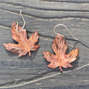 May include: A pair of copper maple leaf earrings with a hammered texture and a silver hook.