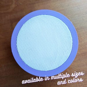 May include: A round, purple-rimmed embroidery hoop with a white fabric center.  Available in multiple sizes and colors.
