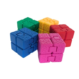 Könnte beinhalten: Vier bunte Fidget Cubes, jeder in einer anderen Farbe: blau, grün, gelb und rot. Die Würfel sind aus Kunststoff und haben eine strukturierte Oberfläche.