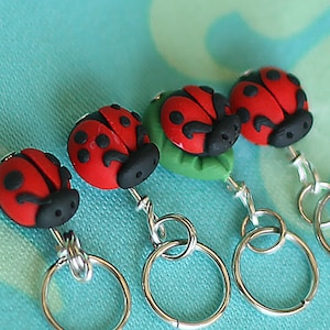 May include: Four ladybug stitch markers with silver rings. The ladybugs are red with black spots and black heads. One ladybug is on a green leaf.