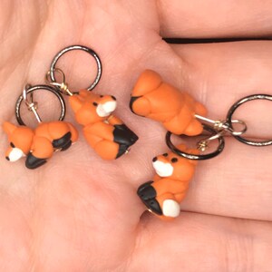 May include: Four orange and black fox stitch markers with silver rings. The foxes are curled up in a sleeping position.
