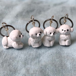 May include: Four white ceramic dog charms with black eyes and noses, each attached to a silver key ring.