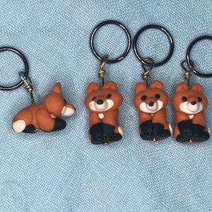 May include: Four fox-shaped stitch markers with black rings. The foxes are brown with black legs and white faces.