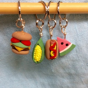 May include: Four colorful food-themed stitch markers, including a hamburger, corn on the cob, hot dog, and watermelon slice. The markers are attached to silver rings and are made of polymer clay.