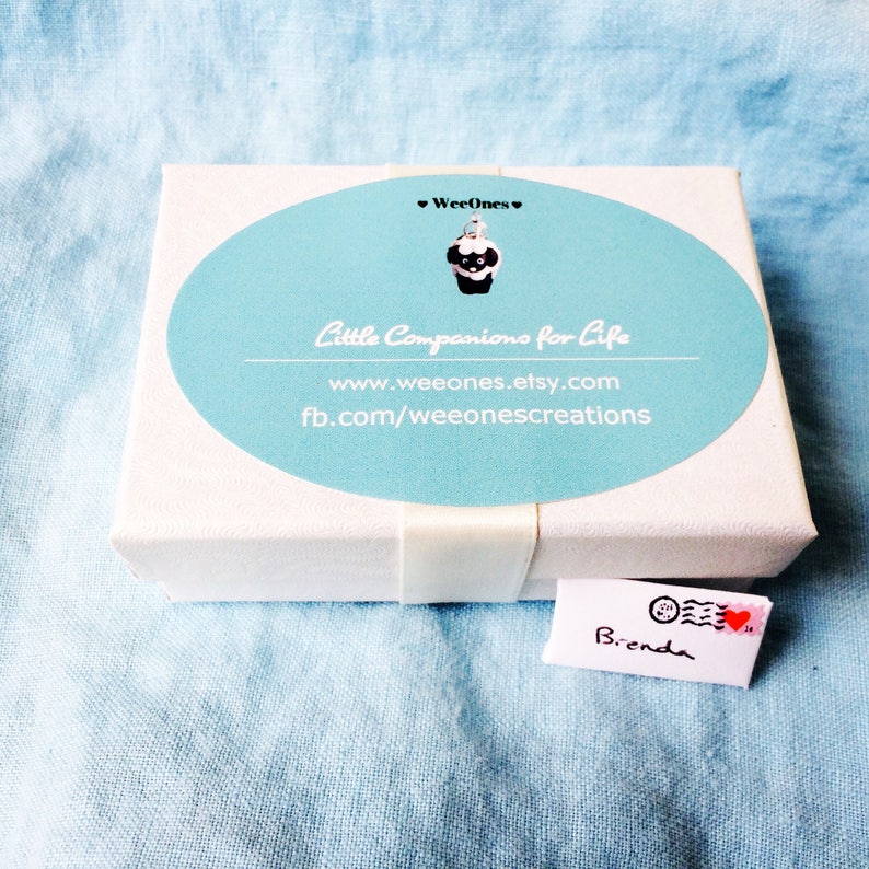 May include: A white box with a blue and white sticker that says "WeeOnes Little Companions for Life" with the website address "www.weeones.etsy.com" and the Facebook page address "fb.com/weeonescreations". A small white envelope with the name "Brenda" written on it is in the bottom right corner of the image.