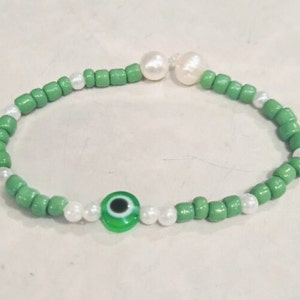 May include: A green and white beaded bracelet with a green evil eye charm and two white pearl beads.