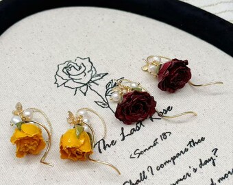 Könnte beinhalten: Goldfarbene Ohrringe mit getrockneten gelben und burgunderfarbenen Rosen, akzentuiert mit Perlen. Die Ohrringe werden auf einer Leinwand mit handgeschriebenem Text aus einem Gedicht präsentiert. The Last Rose <Sonnet 18>.