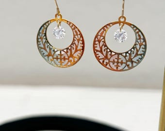 Könnte beinhalten: Ein Paar goldfarbene Filigran-Creolen mit einem kleinen, klaren Edelstein in der Mitte jedes Reifens. Die Ohrringe hängen an goldfarbenen Haken. Das Filigran-Design hat ein Blumenmuster.