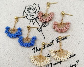 Könnte beinhalten: Handgefertigte Ohrringe aus blauen, rosa und weißen Perlen mit fächerförmigem Design und goldfarbenen Metallakzenten. Die Ohrringe werden auf einem Stoff mit dem Text "The Last Rose" präsentiert.