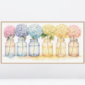 Puede incluir: Una impresión en acuarela enmarcada que presenta seis frascos de vidrio, cada uno con una flor de hortensia de diferente color. Las flores varían del rosa al azul al amarillo, con agua y tallos visibles en los frascos. La obra de arte tiene una paleta de colores pastel suave.